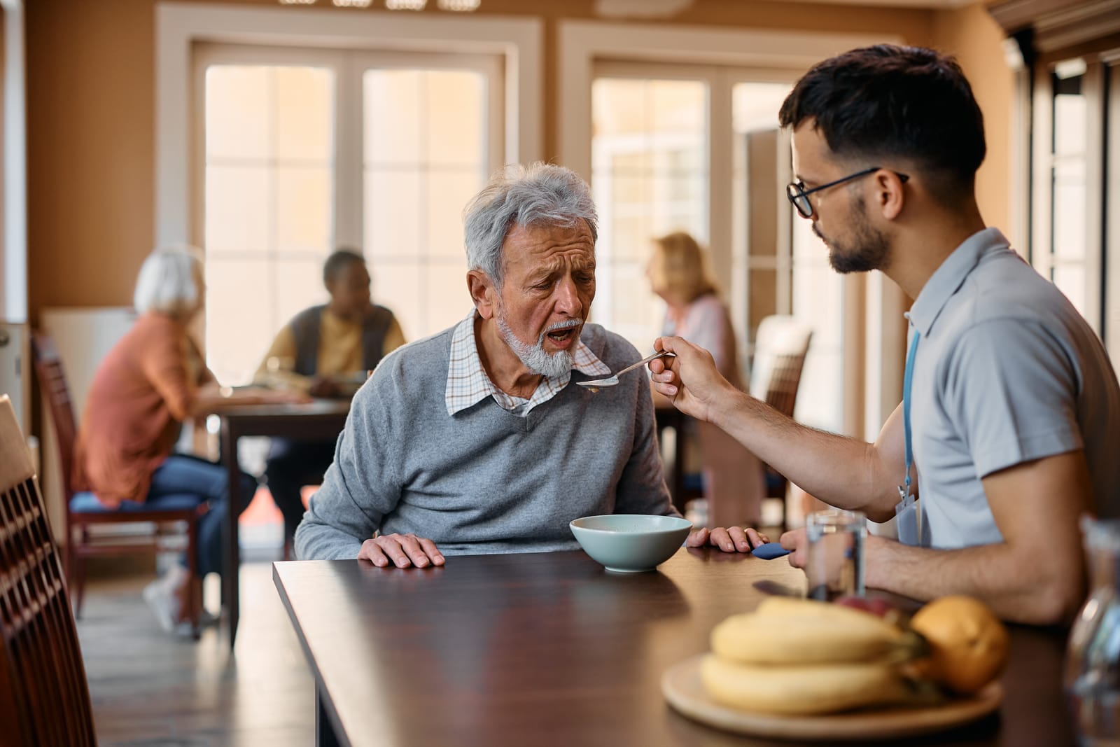 A care professional patiently assisting a senior man during mealtime in a care facility